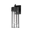Maxim Lighting Millennial Outdoor Wall Sconce in black aluminum with glass shade, mounted on a brick wall, illuminating a patio area.